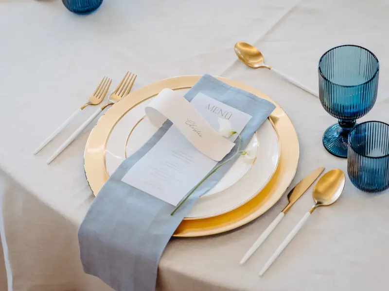Gedeckter Tisch mit goldenem Platzteller und blauen Gläsern